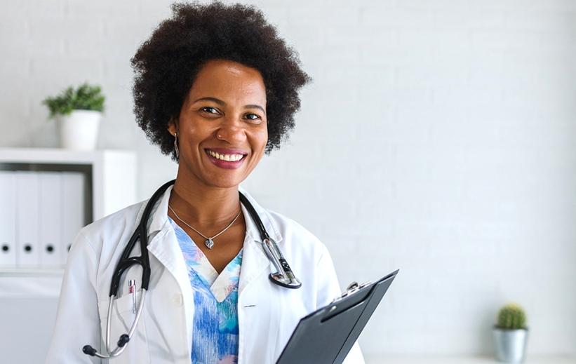 A nurse in a white coat holding a clipboard smiles